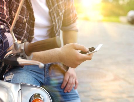 Young man sitting on scooter and using smart phone