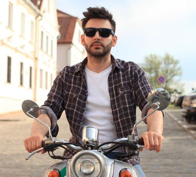 fashionable young man riding a vintage scooter in the street