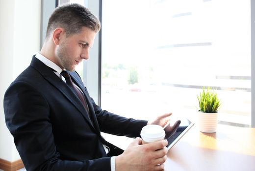 Modern businessman drinking coffee in the office cafe during lunch time and using tablet