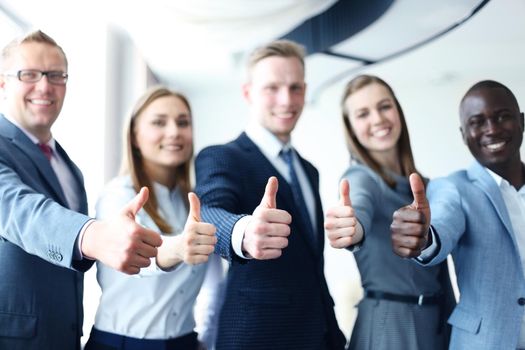 Portrait of happy businesspeople standing in office showing thumb up