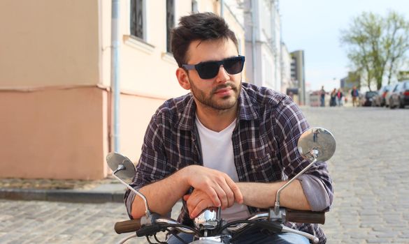 fashionable young man riding a vintage scooter in the street