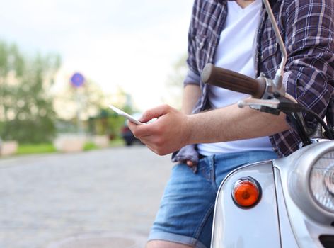 Young man sitting on scooter and using smart phone