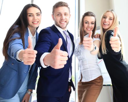 Portrait of happy businesspeople standing in office showing thumb up