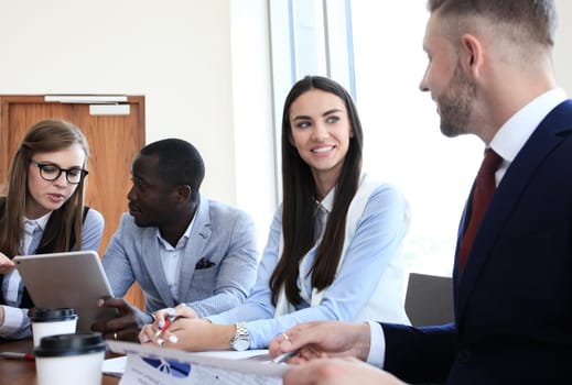 Young handsome man gesturing and discussing something while his coworkers listening to him sitting at the office table