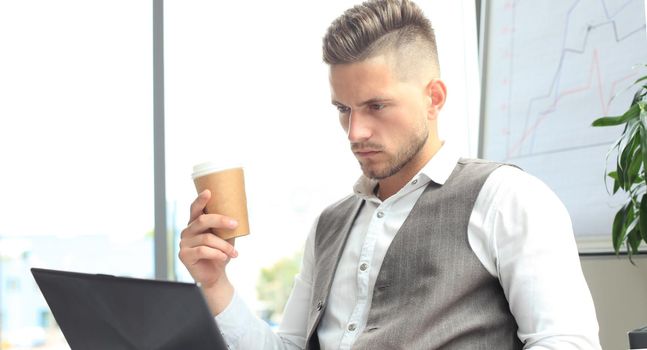 Modern businessman drinking coffee in the office cafe during lunch time and using laptop