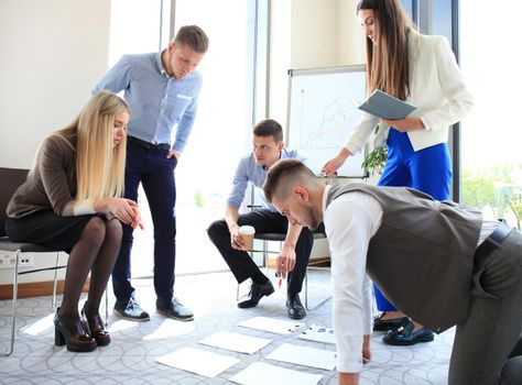 Creative people looking at project plan laid out on floor. Business associates discussing project plan in modern office.