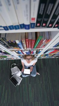 female student study in school library, using tablet and searching for information’s on internet. Listening music and lessons on white headphones