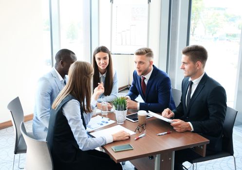 Young handsome man gesturing and discussing something while his coworkers listening to him sitting at the office table