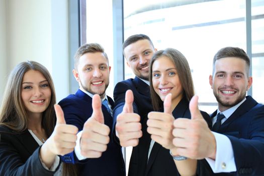 Portrait of happy businesspeople standing in office showing thumb up