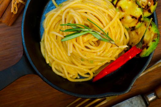 italian spaghetti pasta with zucchini sauce on iron skillet over wood board