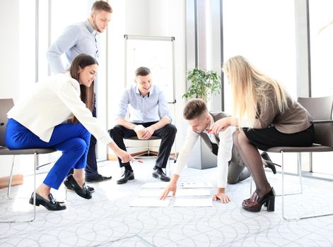 Creative people looking at project plan laid out on floor. Business associates discussing new project plan in modern office.