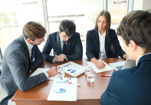 Young handsome woman gesturing and discussing something while his coworkers listening to him sitting at the office table