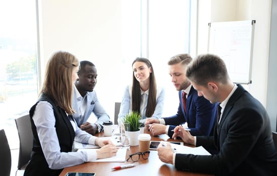 Young handsome man gesturing and discussing something while his coworkers listening to him sitting at the office table