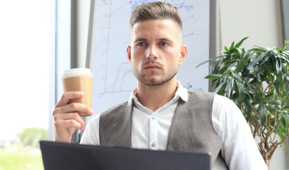 Modern businessman drinking coffee in the office cafe during lunch time and using laptop