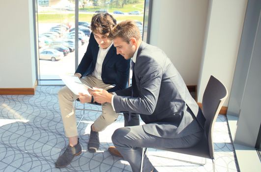 Mature businessman using a digital tablet to discuss information with a younger colleague in a modern business office.