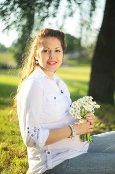 Beautiful pregnant woman relaxing outside in the park with flowers camomile in the hands