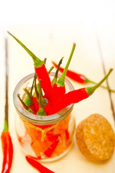 red chili peppers on a glass jar over white wood rustic table