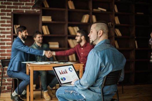 financial administrator works with financial graphs on the background of business partners handshaking in a modern office