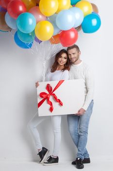 Young smiling couple with balloons and big gift box, Valentine day birthday surprise concept