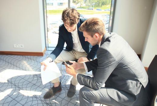 Mature businessman using a digital tablet to discuss information with a younger colleague in a modern business office.