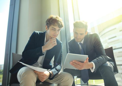 Mature businessman using a digital tablet to discuss information with a younger colleague in a modern business office.