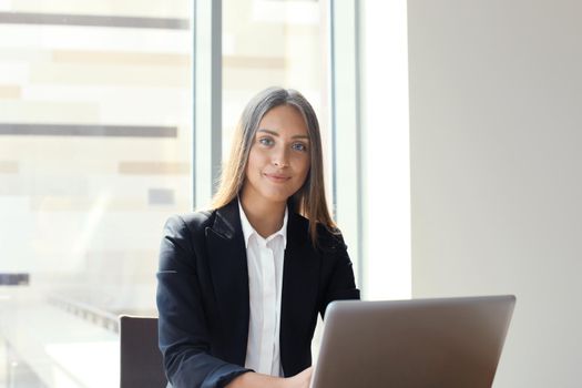 Portrait of a cheerful young businesswoman sitting at the table in office and looking at camera.