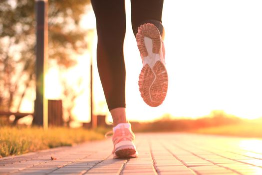 Runner feet running on road closeup on shoe, outdoor at sunset or sunrise.