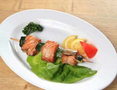 skewers of salmon with garnish on white plate on wooden backgrou