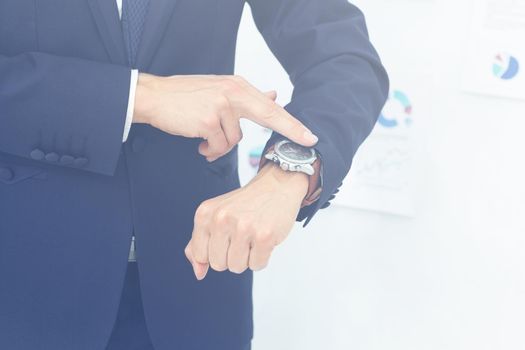 on the left side of the photo close-up of businessman with finger point at his watch in his hand. on the right side of the photo on the background of the financial schedules there is empty space for your text