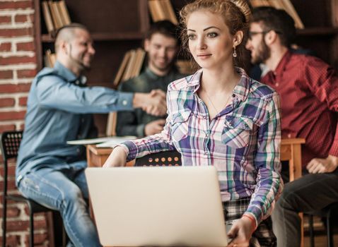 young successful financial administrator woman with laptop on background of business partners handshaking