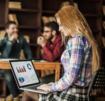 sales Manager working on laptop with a marketing report on the background of business team in a modern office