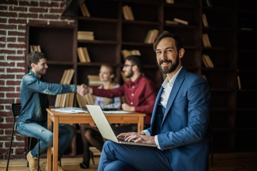 Manager Finance works with the marketing graphics on the laptop on the background of business partners handshaking in the workplace in the office