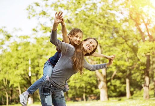 happy mother with her daughter in the park on a sunny day, imitating the flight of the aircraft