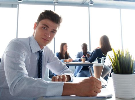 Young businessman standing in office with his collegue on the background