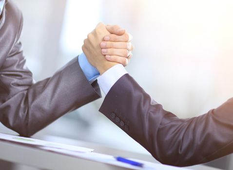 Two businessmen press hands with each other in the foreground. Fighting between entrepreneurs. armwrestling