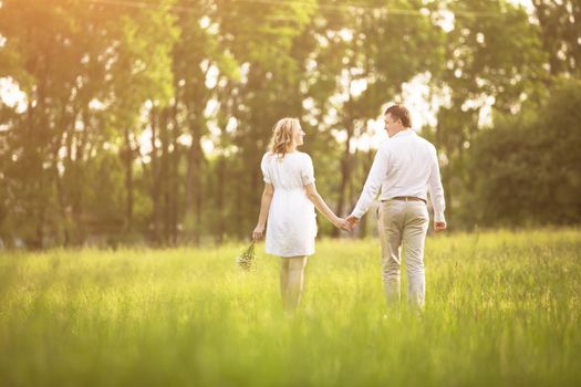 Happy couple - pregnant woman and her husband go on a picnic on the grass. They look at each other