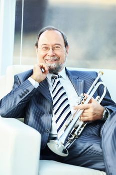 Portrait of a musician with a pipe, sitting on a chair, smiling and supports beard hand