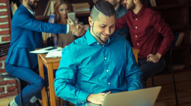 employee of the company with laptop on background of business partners handshaking in a modern office