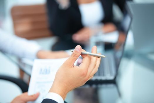 closeup hand of businessman holding a pen and works with financial graph on background of office