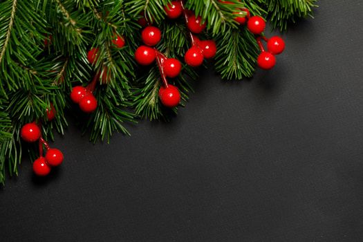Christmas border arranged with fresh fir branches and red berries on black paper background , copy space for text
