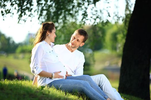 pregnant woman and happy future father sitting on the grass in the Park on a Sunny day