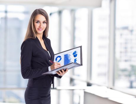 Young, attractive, successful business woman, studying charts, smiling and looking at the frame