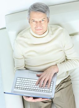 Happy elderly man at home with laptop on sofa looking up