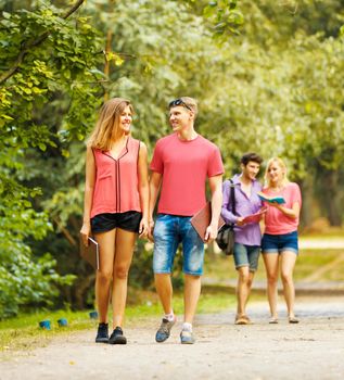 Group of happy students in a park on a sunny day are on the road and discuss training