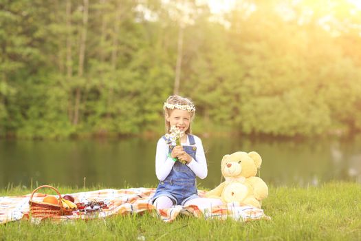 little girl with a soft toy on a picnic near the river on a Sunny day