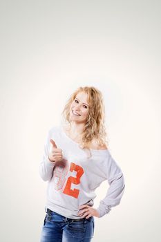 Beautiful young blond woman in jeans and t-shirt showing a thumbs up on a white background