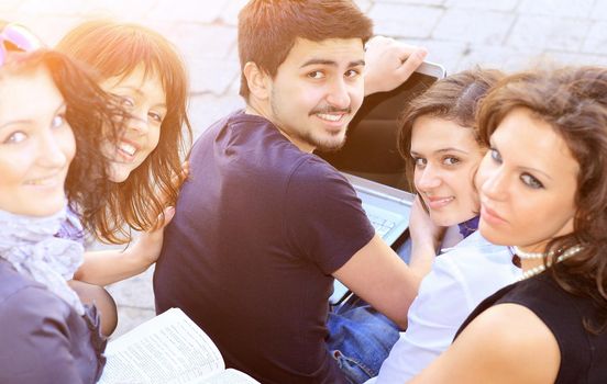 Group of cheerful students with a laptop on a college background on a sunny day