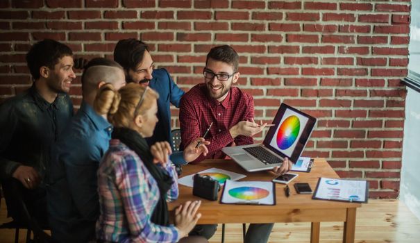 team of designers in the workplace in front of the open laptop is discussing a new color palette in a modern office