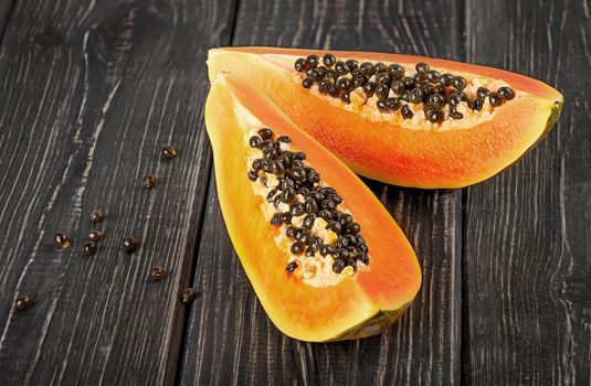 Two pieces of ripe papaya on a wooden table. Quarters of papaya on a dark plank table.