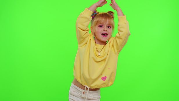 Dancing young little kid girl blogger record dance moves at camera for social media content using phone indoors on chroma key green screen background. Children schoolgirl perform trendy funny dance